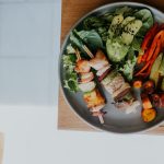 Top view of a vibrant platter with grilled skewers and fresh vegetables on a wooden table.