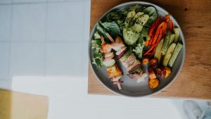 Top view of a vibrant platter with grilled skewers and fresh vegetables on a wooden table.
