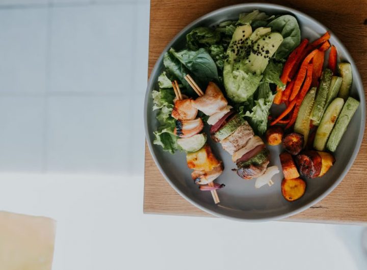 Top view of a vibrant platter with grilled skewers and fresh vegetables on a wooden table.